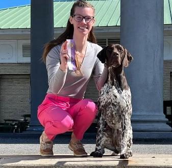 Abby crouching beside a German shorthaired pointer, holding a show ribbon