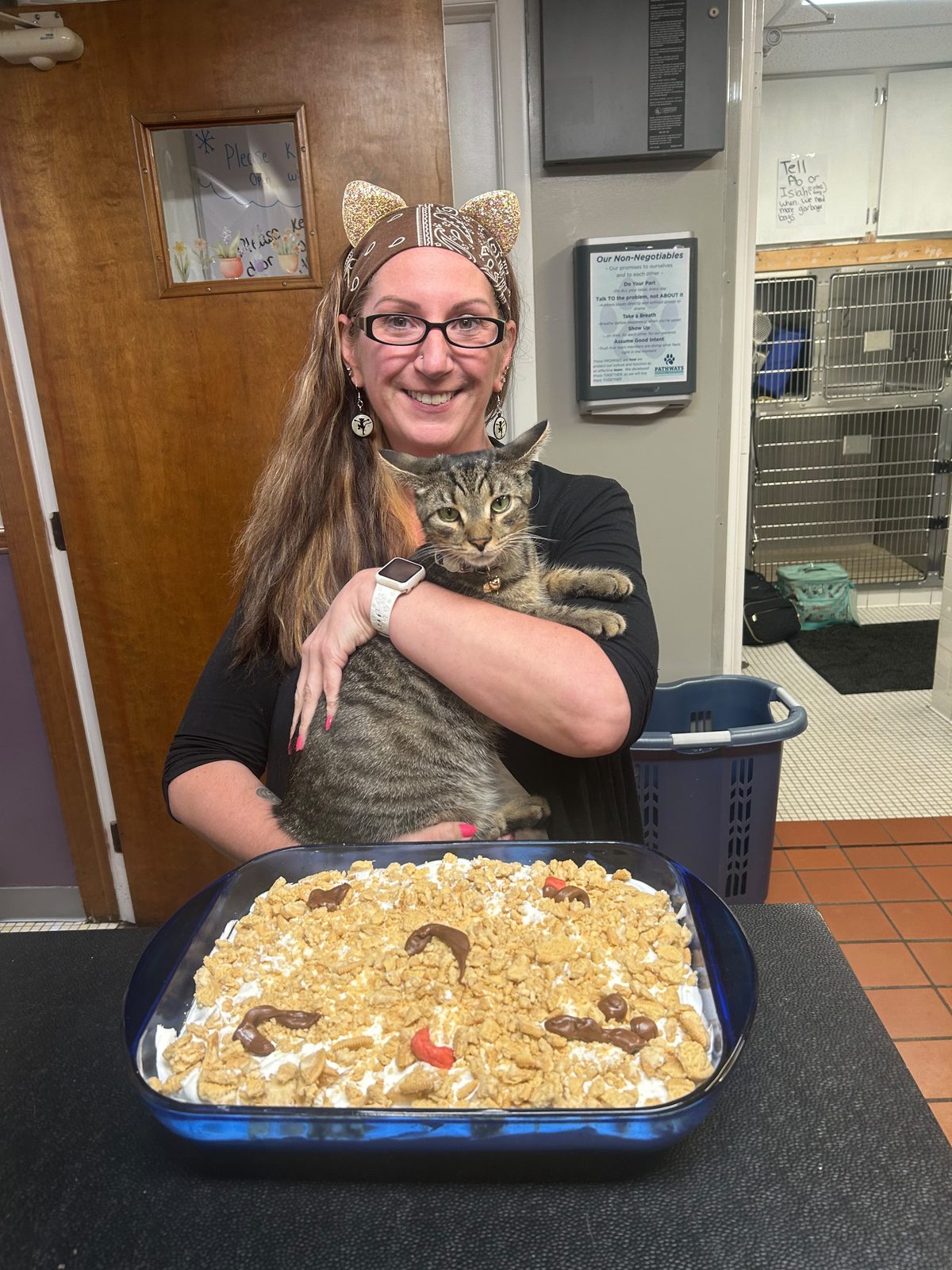 Charleen holding a cat at the reception desk beside a tray of food