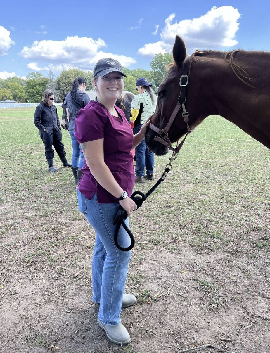 Ella in a riding helmet holding a horse on a lead rope in a field